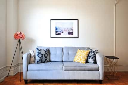 A living room setting featuring a grey couch with four pillows on it and a picture behind it on the wall.