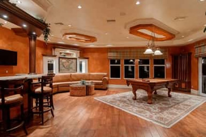 A fancy looking room with a bar, a pool table and a nice area rug underneath it.  There is also nicely upholstered furniture.